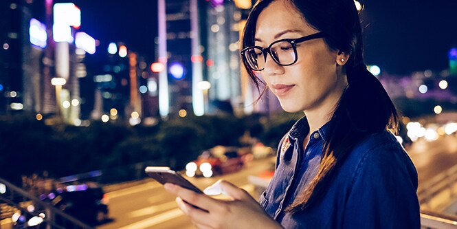 Zdjęcie kobiety korzystającej z urządzenia mobilnego w mieście nocą.
