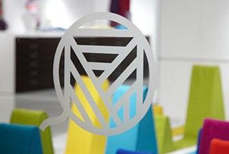 Okno z wytrawionym szkłopodobnym logo graficznym i kolorowymi kształtami z tyłu.
