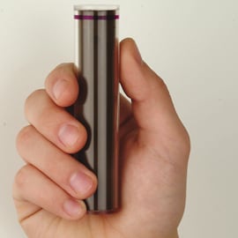 Ręka trzyma smukły, cylindryczny metalowy przedmiot z cienkim fioletowym paskiem u góry.