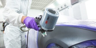 lakiernik natryskujący lakier na samochód za pomocą 3M Performance pistoletu natryskowego 
