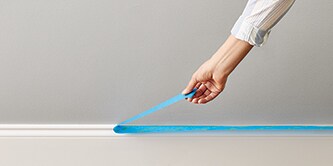 Osoba usuwająca taśmę malarską ScotchBlue™ z listwy przypodłogowej
