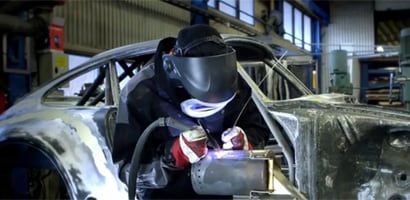 Obraz przedstawiający spawacza ubranego w odzież ochronną i używającego palnika spawalniczego na metalowej konstrukcji w zakładzie produkcyjnym
