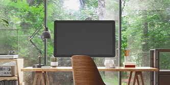 Monitor na biurku, w tle widoczny jest las
