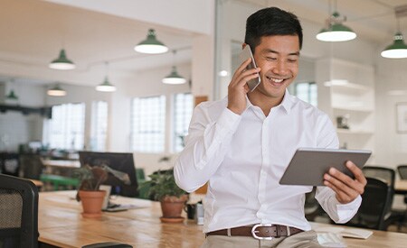 Obraz uśmiechniętego biznesmena rozmawiającego przez telefon i patrzącego na tablet.
