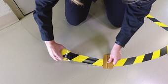 Zdjęcie jak osoba przykleja żółto- czarną taśmę na podłogę.
