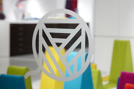 Okno z wytrawionym szkłopodobnym logo graficznym i kolorowymi kształtami z tyłu.
