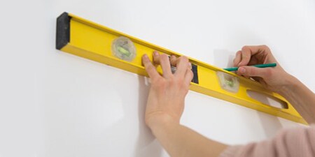 Zdjęcie przedstawiające osobę używającą poziomnicy do zaznaczania obszarów na ścianie
