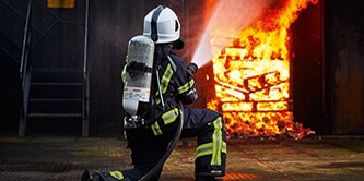 strażak wspinający się po drabinie płonącego domu
