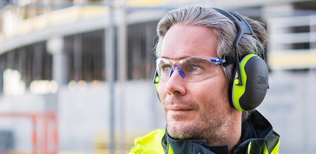 Osoba na placu budowy w żółtej odzieży ochronnej, w słuchawkach przeciwhałasowych 3M.
