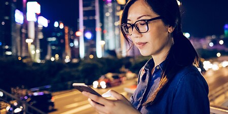 Kobieta korzystająca z urządzenia mobilnego w mieście nocą.
