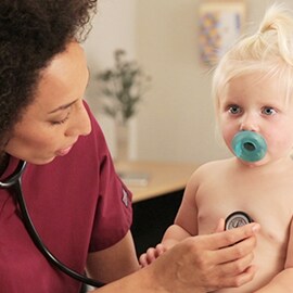 Pielęgniarka pediatrii osłuchująca klatkę piersiową małego dziecka za pomocą Stetoskopu 3M Littmann Classic III.