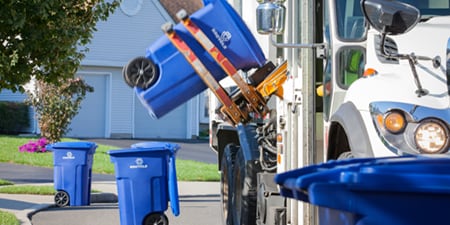 Niebieski pojemnik na odpady do recyklingu jest podnoszony do ciężarówki zajmującej się recyklingiem.
